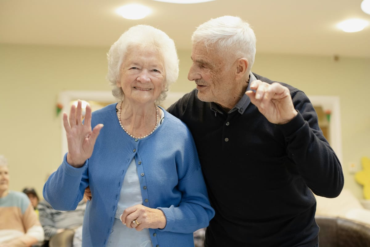 Older couple waving hello in a room
