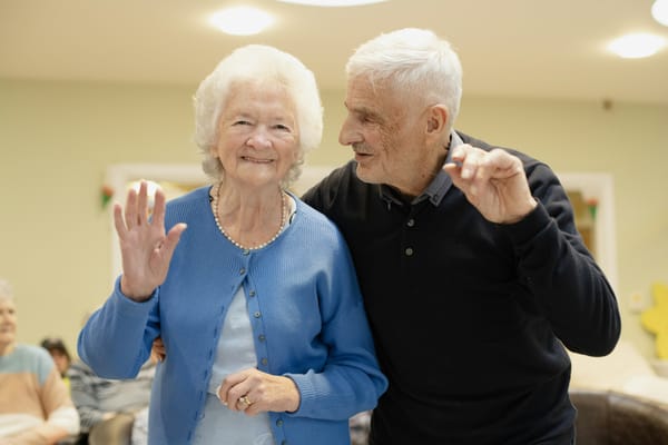 Older couple waving hello in a room